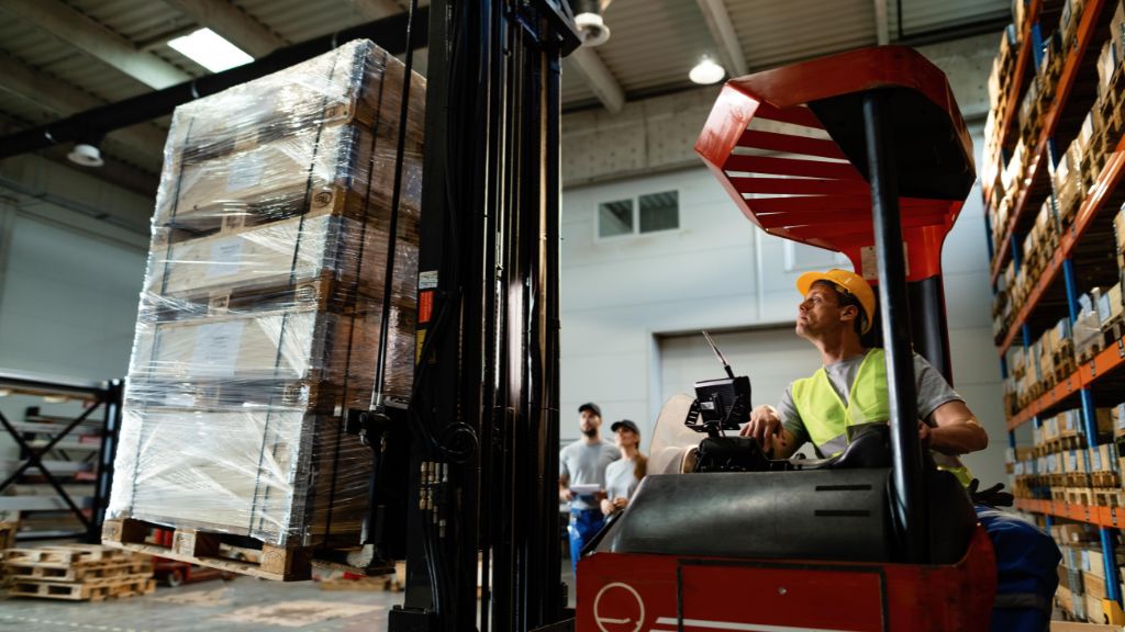 a warehouse worker using a forklift to lift up a loaded pallet